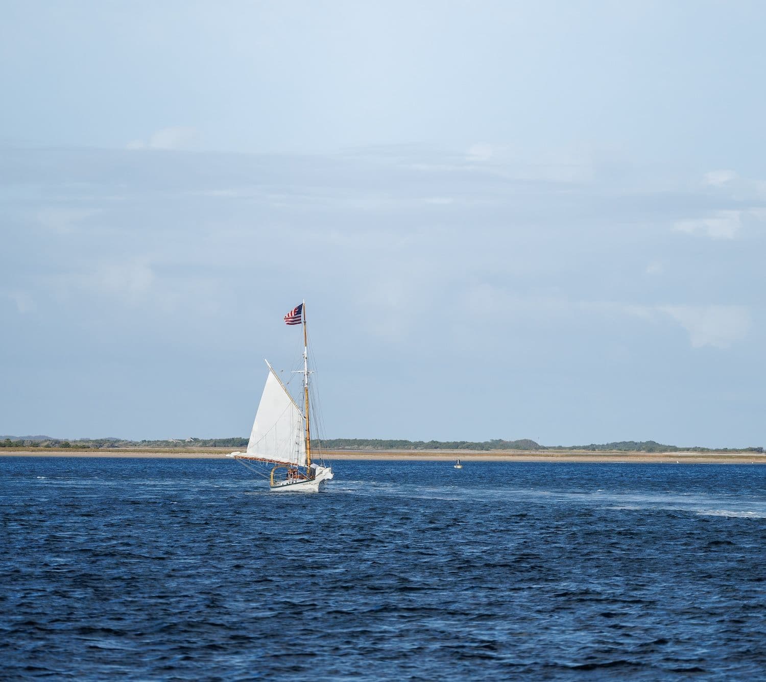Sailboat with American flag in blue water.